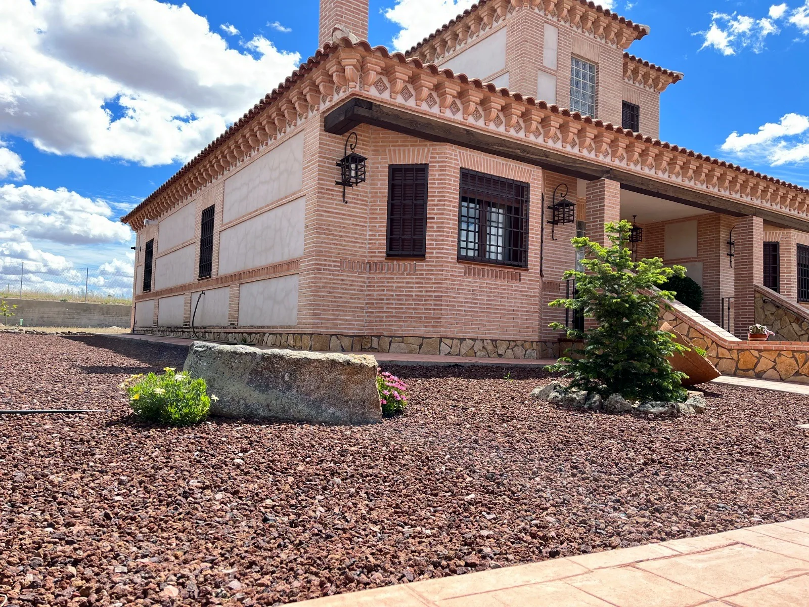 Jardín de bajo mantenimiento con grava volcánica, roca y arbustos frente a un chalet de ladrillo