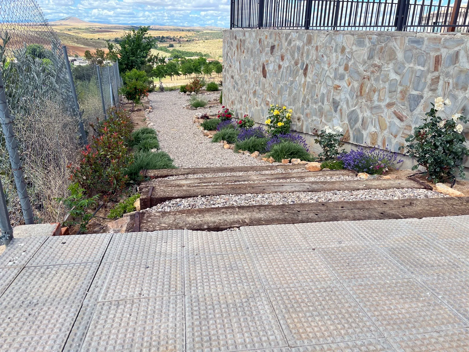Jardín en pendiente con escalones de traviesas, grava y plantas en flor